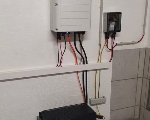 Weißer Wechselrichter an der Wand und ein weißer Batteriespeicher. Der Speicher steht am Boden.
