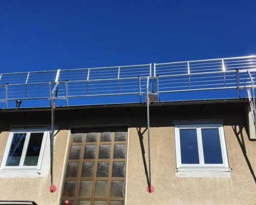 Ansicht eines beigen Hauses. An der Dachkante ist eine Gerüst montiert.